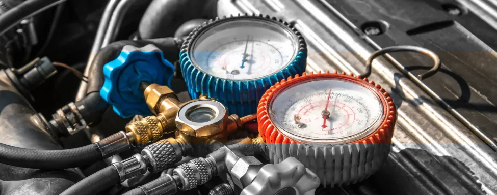 Auto A/C Repair In Sterling, VA At Honest Tom Care. A close-up shot of a mechanic's hands using a set of gauges to check a car's air conditioning system.