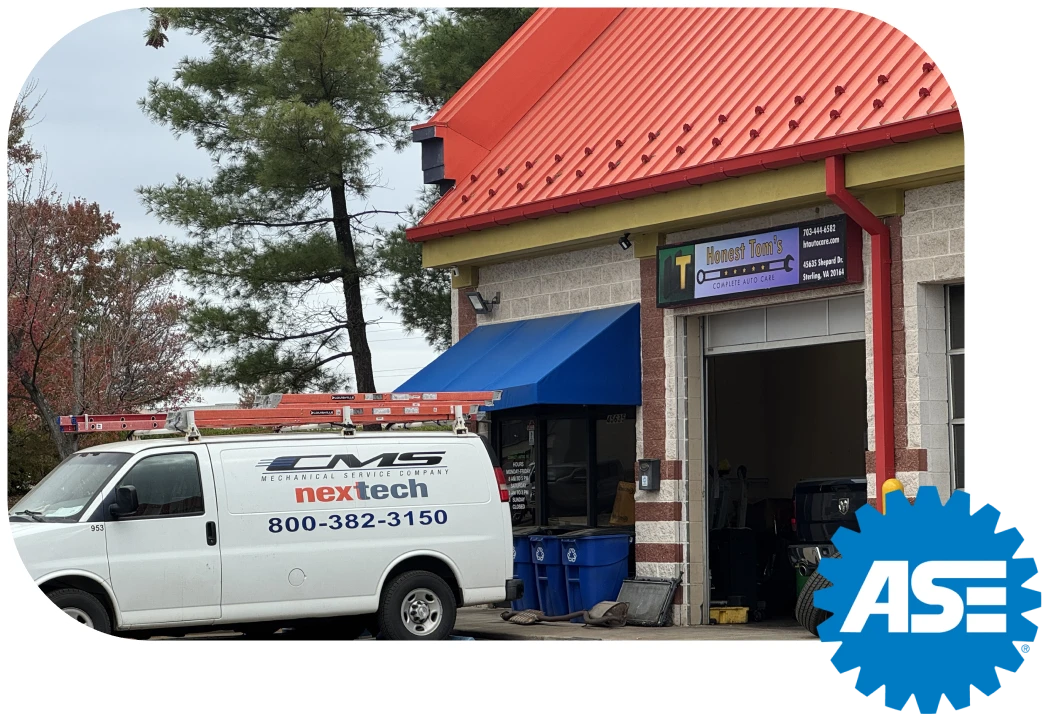 The exterior of an auto repair shop with a red corrugated roof, a blue awning over a window, and the sign Honest Tom's above a large service bay entrance, with a white service van parked in front.