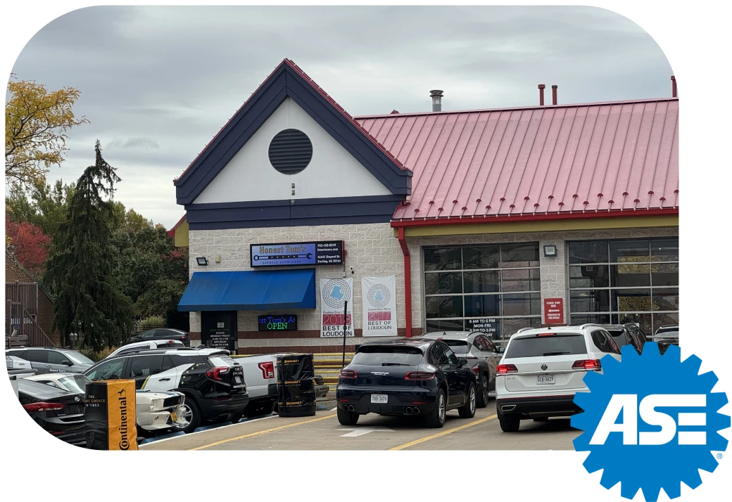 The exterior of a busy auto repair shop with a red shingled roof and a blue awning, showing several cars parked in the lot and banners.