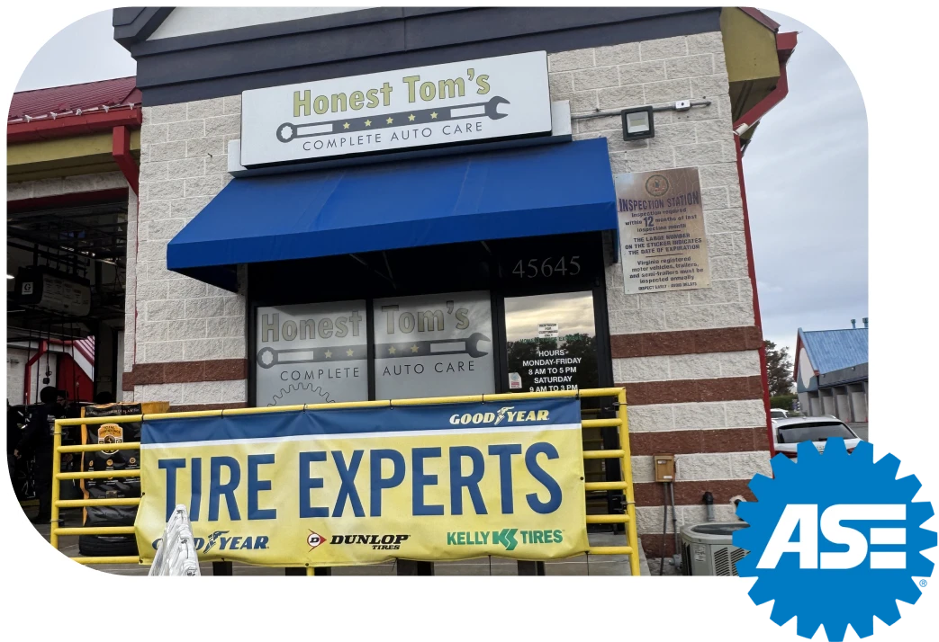 The front of an auto repair shop with light brick siding and a blue awning over the door, displaying a sign for Honest Tom's Complete Auto Care and a large yellow banner that reads Tire Experts.