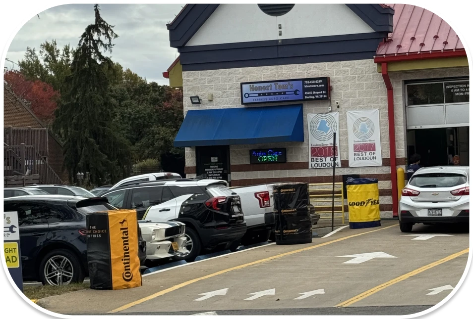 An exterior view of the auto repair shop entrance and parking lot, with several cars parked outside on a cloudy day.