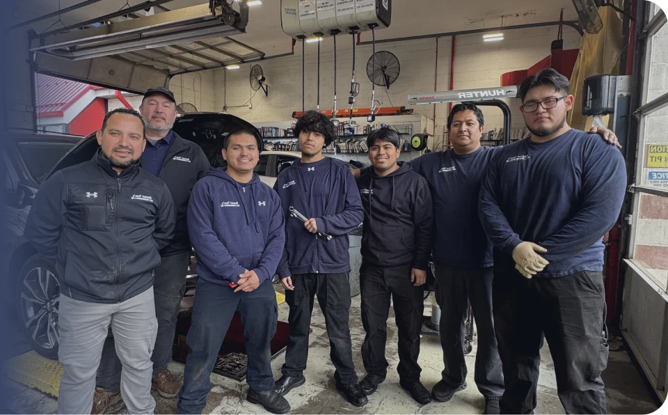 A group of seven mechanics in dark blue uniforms pose for a photo inside a brightly lit garage bay.